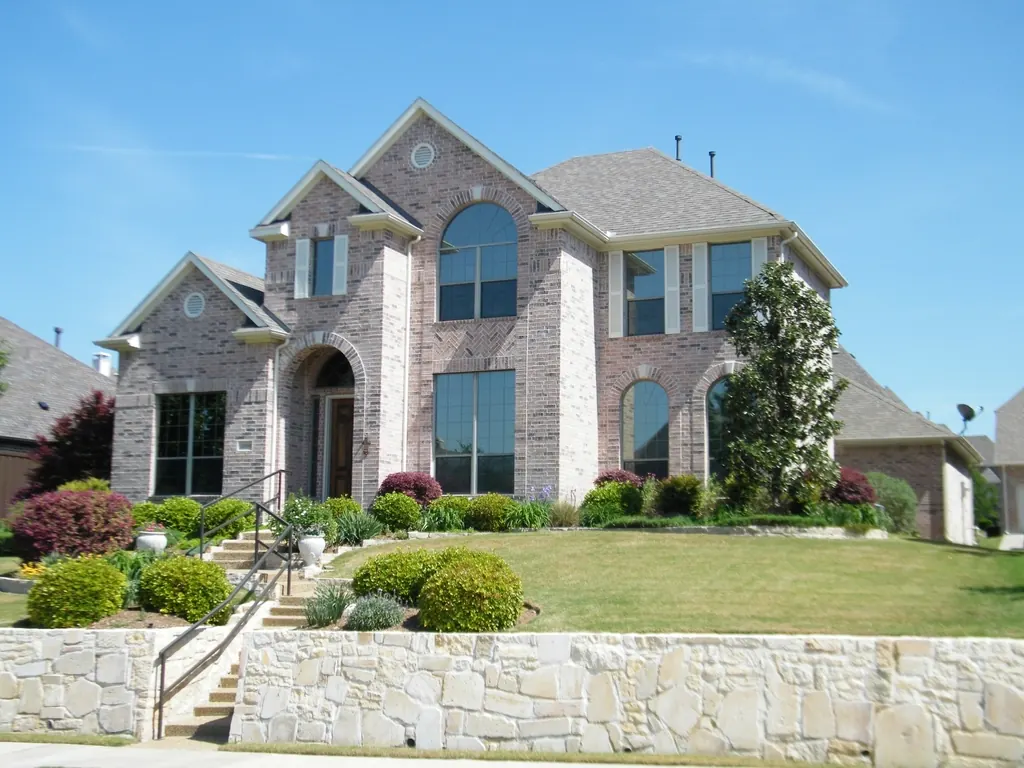 Brick suburban American home with a gray asphalt shingle roof and landscaped front yard