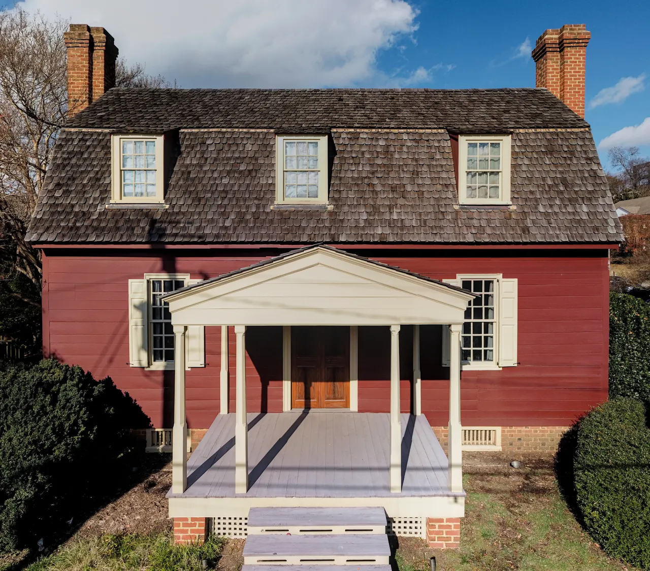 Red colonial-style American house with a shake roof and two brick chimneys